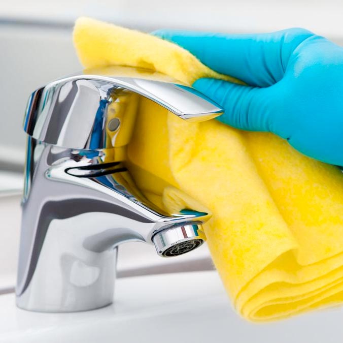 close up photo of a persons hand wearing a glove disinfecting a faucet handle