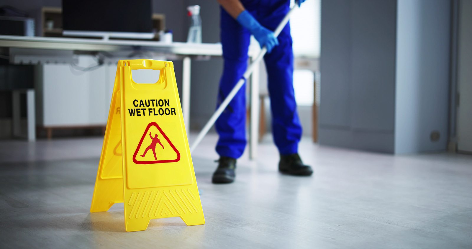 photo of man cleaning office floor with wet floor sign